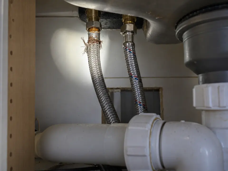 Two braided steel flexi-hoses under a sink, one frayed at its top fitting
